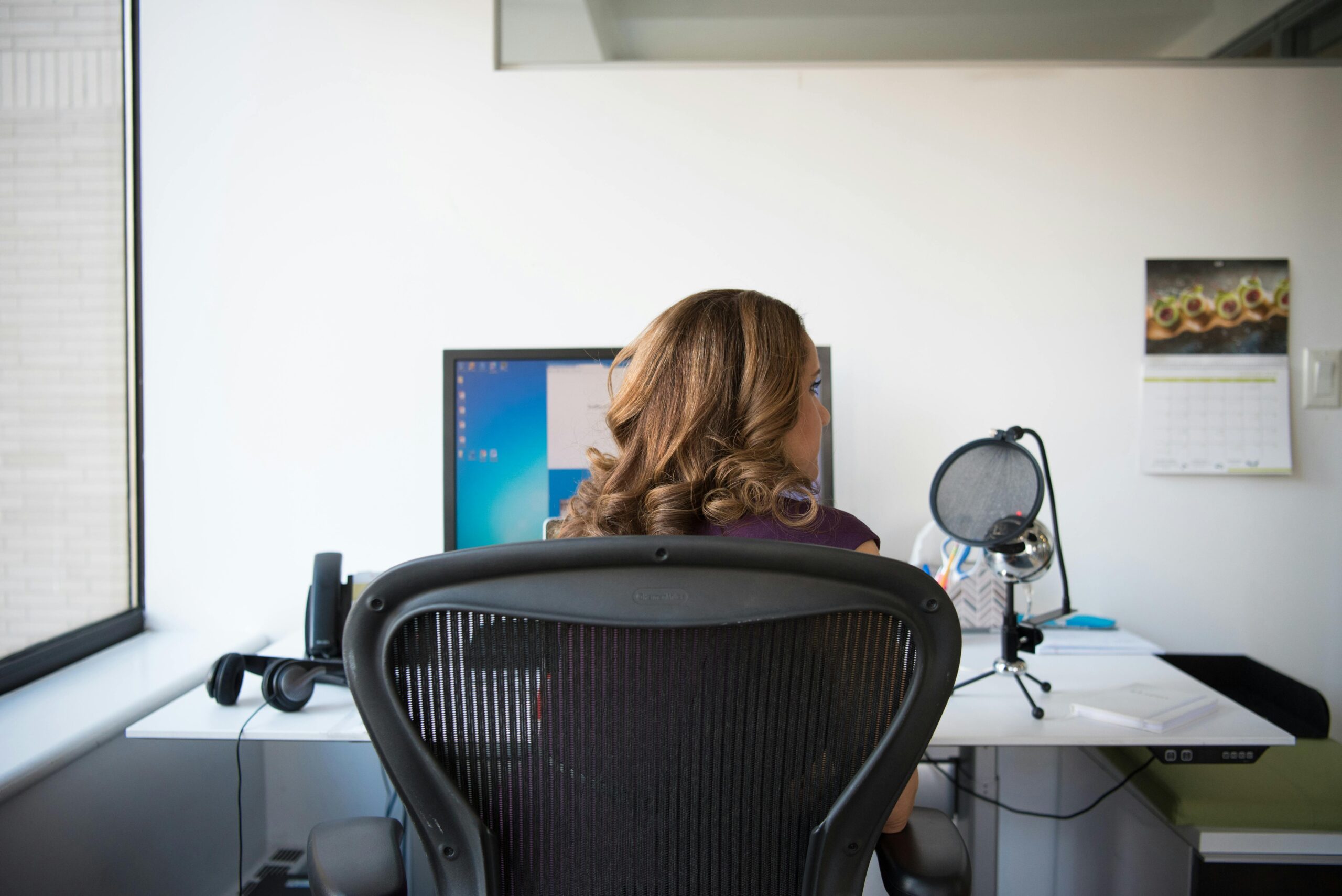 Adult woman working in a contemporary office setting with computer and microphone.