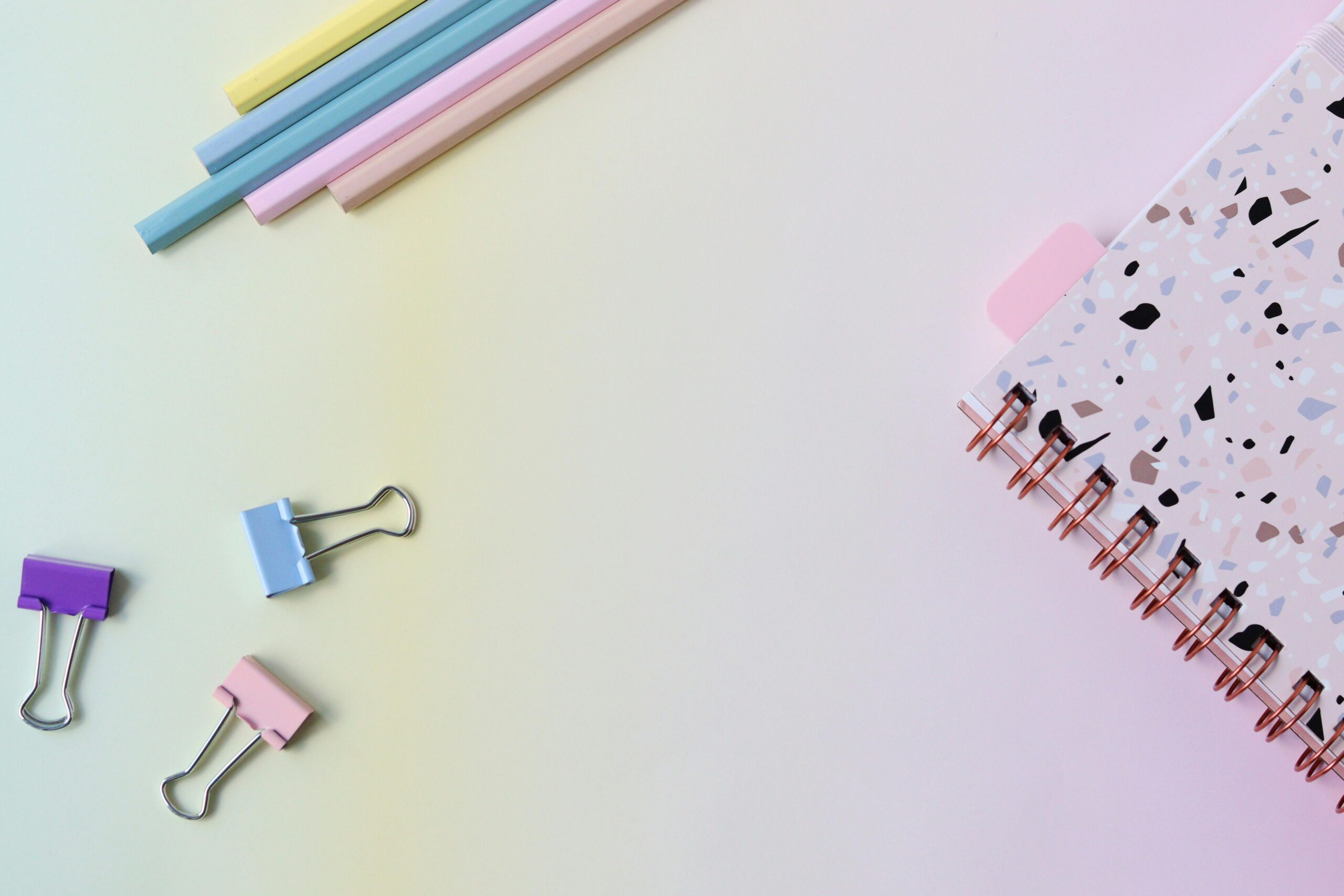 Stylish flat lay of pastel stationery with a notebook and paper clips on a soft background.